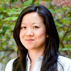 a woman with long black hair wearing a white shirt and smiling at the camera while standing in front of some trees