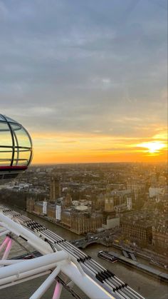 an aerial view of a ferris wheel and the sun setting over london, england in the distance