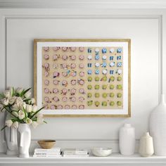 a white shelf with vases and flowers on it next to a framed art piece