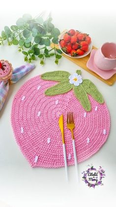 a crocheted placemat with flowers and leaves on it next to a plate of strawberries