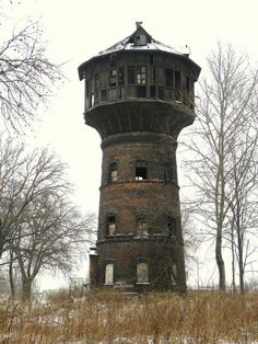 an old water tower sitting on top of a snow covered hill next to trees and bushes