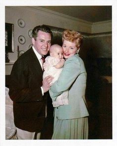 a man in a suit holding a baby and smiling at the camera while standing next to a woman