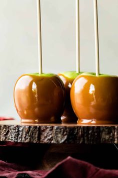 two caramel apples with white sticks sticking out of them on a wooden tray next to a red cloth