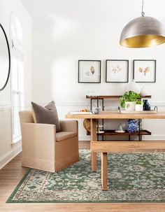 a dining room table and chairs in front of pictures on the wall above it, with a green rug underneath