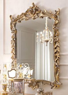 an ornate gold framed mirror on the wall above a small table with a candle holder