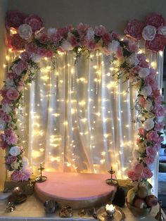 a table topped with a cake covered in pink flowers and greenery next to a white curtain