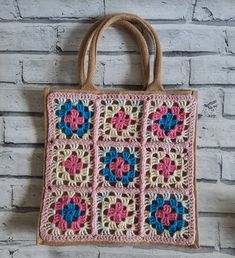 a crocheted bag hanging on a brick wall with flowers in the center and two handles