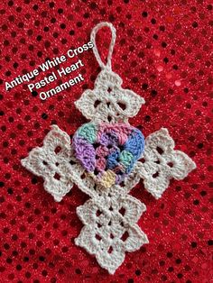 a crocheted ornament is shown on a red surface with the words antique white cross, pastel heart ornament