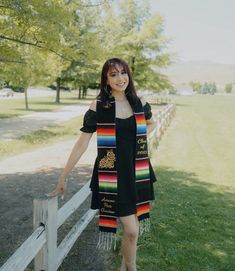 a woman standing next to a wooden fence wearing a black dress and colorful shawl