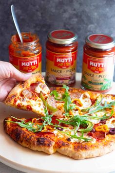 a person holding a slice of pizza on a plate with three jars in the background