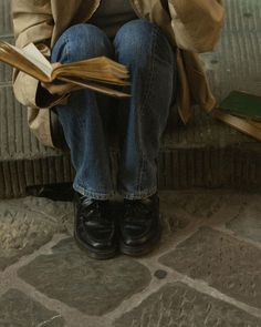 a person sitting down reading a book on the ground with their legs crossed and holding an open book