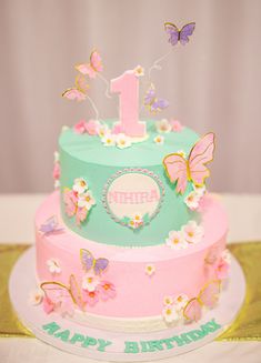 a birthday cake decorated with butterflies and the number one on top is pink, blue, and green