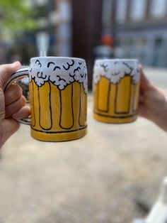 two people holding up mugs with foamy beer on them in front of a building