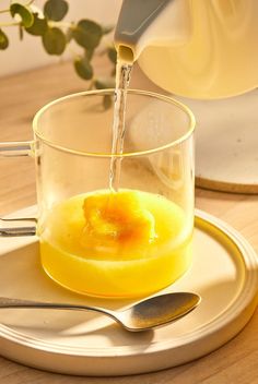 a glass cup filled with liquid on top of a wooden table next to a spoon