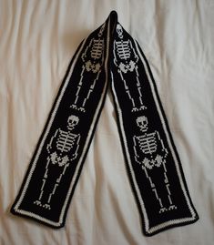 two black knitted scarves with white skulls and bones on them sitting on a bed