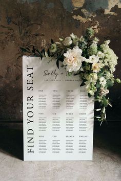 a seating chart with flowers and greenery is displayed in front of an old wall