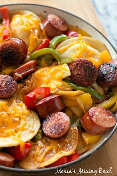 a pan filled with sausages, potatoes and peppers on top of a wooden table