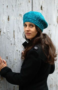 a woman wearing a blue hat standing next to a white wall with peeling paint on it