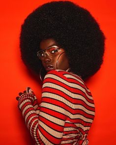 a woman with an afro wearing glasses and a red striped sweater is posing for the camera