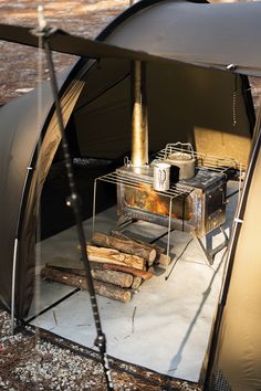 an outdoor stove and some logs in a tent with the door open to show it's cooking area