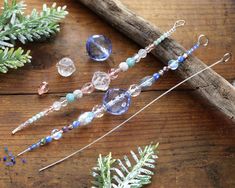 some beads and needles are laying on a wooden table next to pine cones, twigs and branches