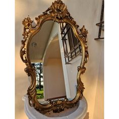 an ornate gold framed mirror sitting on top of a white pedestal