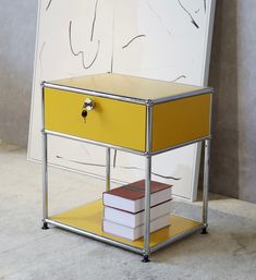 a yellow table with two books on it and a white wall behind it, in front of a painting