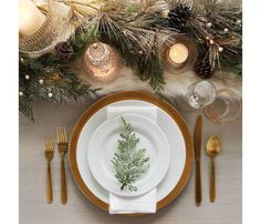 a place setting with pine cones, candles and greenery on the table for christmas dinner