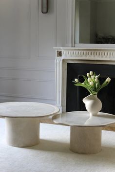 two white tables with flowers on them in front of a fireplace