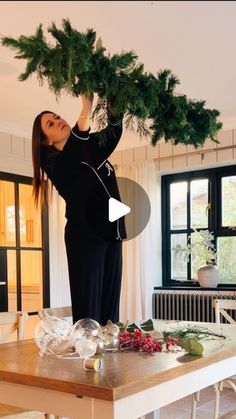 a woman standing on top of a wooden table holding a christmas tree over her head