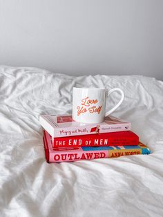 a stack of books sitting on top of a bed next to a cup with the words i love you so much