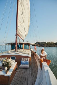 a man and woman sitting on the deck of a sailboat looking out at the water