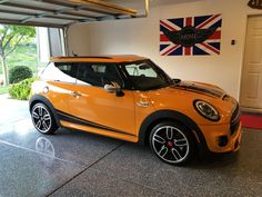 an orange mini cooper in a garage with the british flag on the wall behind it