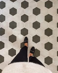 a person wearing black shoes standing in front of a tiled floor with hexagonal tiles