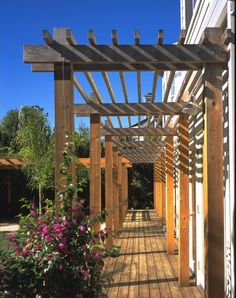 a wooden pergolated walkway next to a building with flowers growing on the side