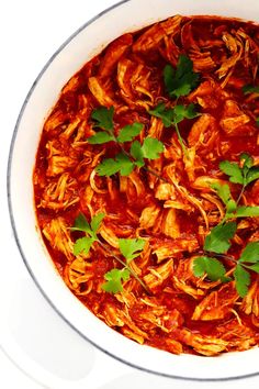 a white bowl filled with shredded meat and garnished with parsley on top