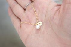 a person's hand holding a tiny gold necklace with two pearls on the end