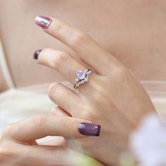 a woman's hand with purple and white nail polish holding a ring on her finger