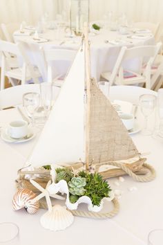 a small sailboat is sitting on top of a table with seashells and succulents