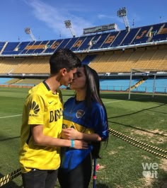 a young man and woman standing next to each other in front of a soccer field