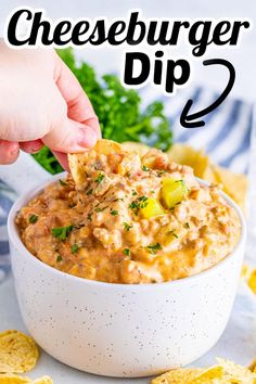 a hand dipping cheeseburger dip into a white bowl with crackers on the side