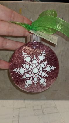 a hand holding a glass ornament decorated with white dots and a green ribbon