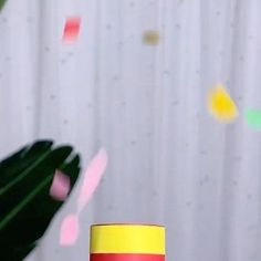 a red and yellow coffee cup sitting on top of a table next to a plant