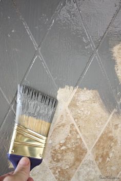 a person holding a paint brush in front of a wall with diamond tiles on it