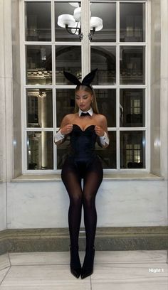 a woman is posing in front of a window wearing bunny ears and black tights