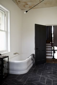 a bath tub sitting next to a black door in a white room with tile flooring