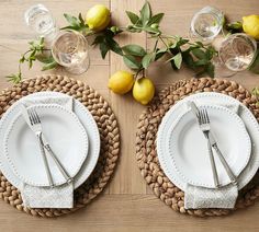 two plates with silverware are sitting on a placemat next to lemons and greenery