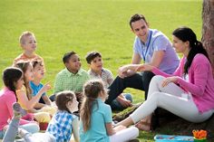 a group of people sitting on the ground next to a tree in a park, talking