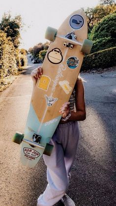 a person holding a skateboard with stickers on it's face while walking down the street