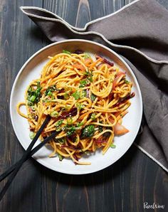 a white plate topped with noodles and vegetables on top of a wooden table next to a fork